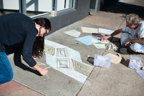 Outside of Spark Gallery in the Santa Fe Arts District, artists draw chalk art on the sidewalk.