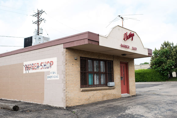 Charley's Barbershop, a small, standalone brick building with cursive red writing and a matching red door, facing the eastward traffic of I-70.