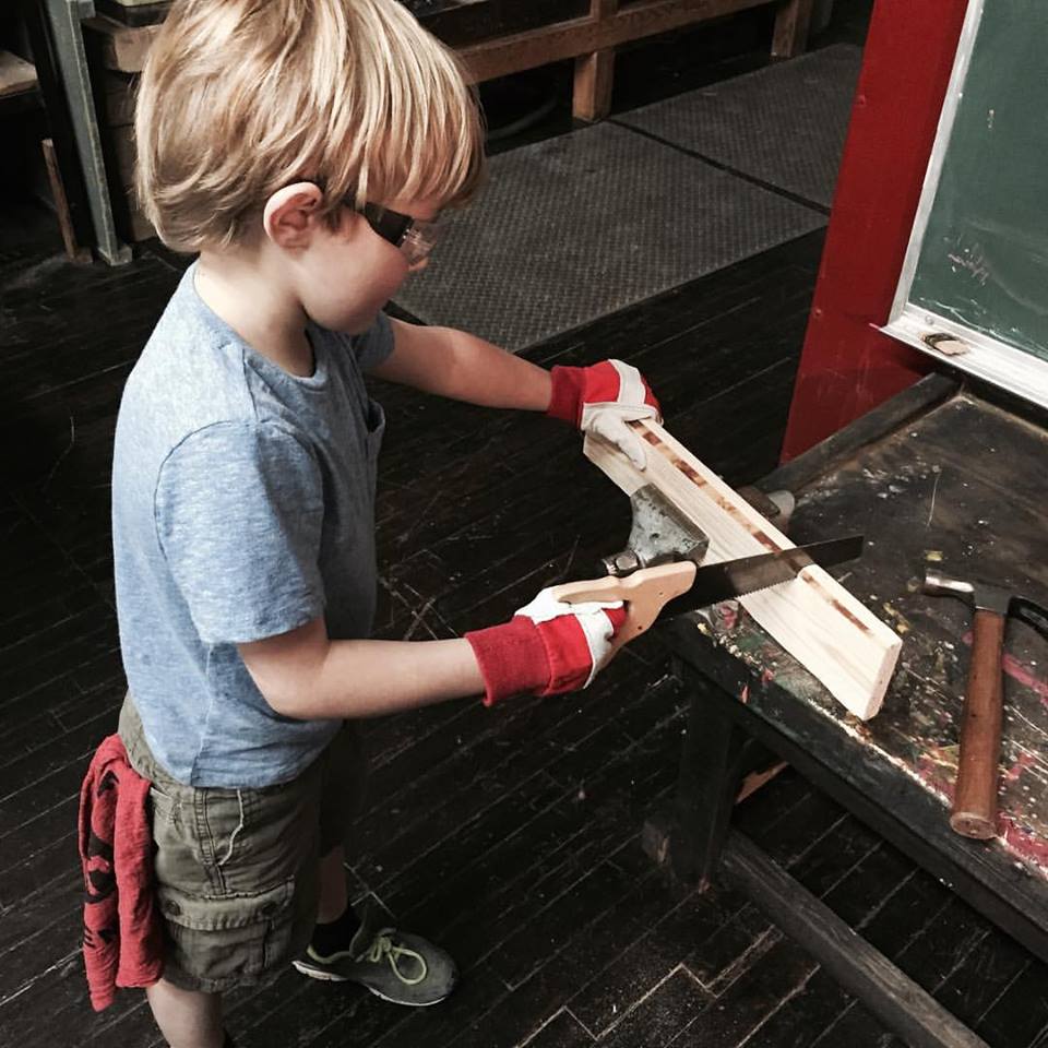 A child saws away at Craftsman & Apprentice.