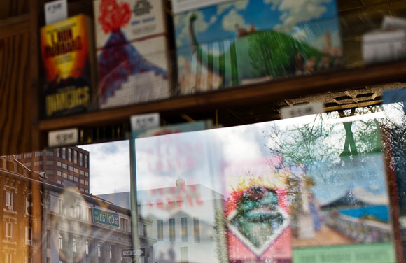 A Colfax street sign is reflected in the windows of a bookstore. 